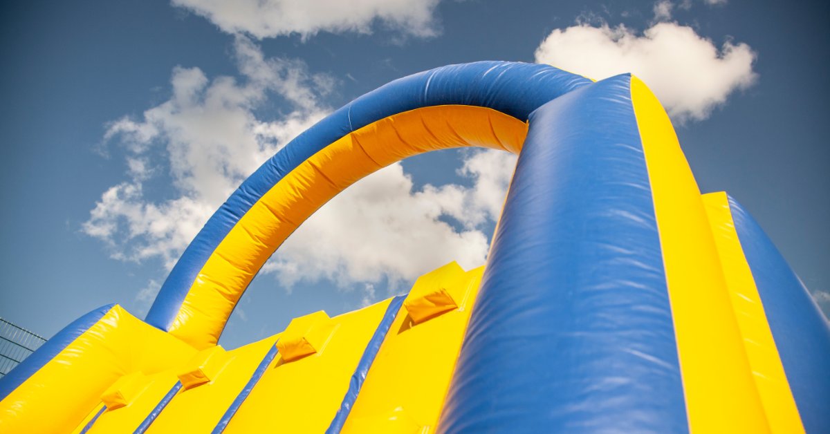 A large inflatable climbing wall installed outside during the daytime. The inflatable is colored yellow and blue.