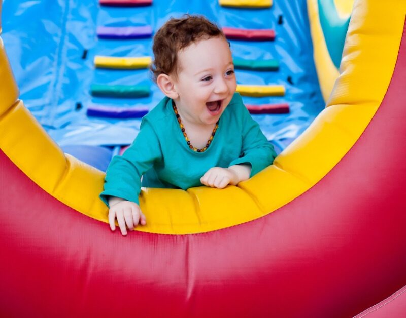 A toddler wearing a light blue shirt smiling while crawling to the end of an inflatable obstacle course.