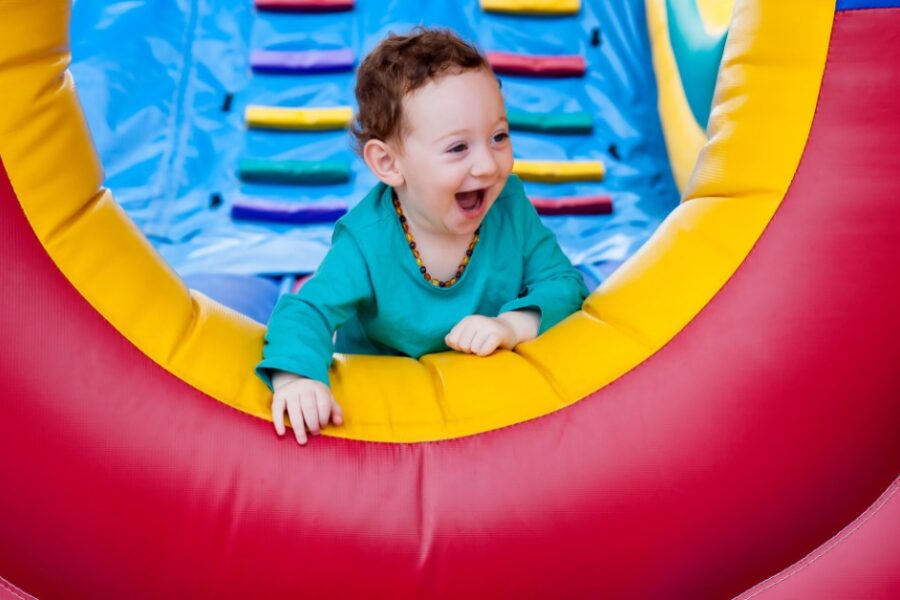 A toddler wearing a light blue shirt smiling while crawling to the end of an inflatable obstacle course.