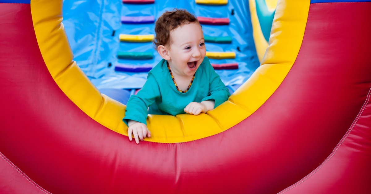A toddler wearing a light blue shirt smiling while crawling to the end of an inflatable obstacle course.