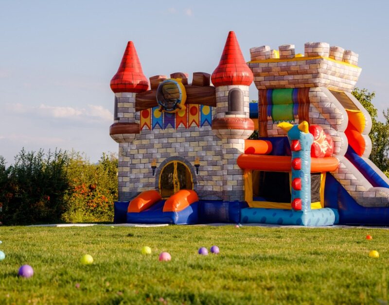 A tall bounce house shaped like a castle. The bounce house is surrounded by colorful balls outside during the daytime.