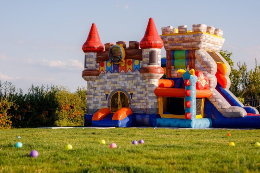 A tall bounce house shaped like a castle. The bounce house is surrounded by colorful balls outside during the daytime.