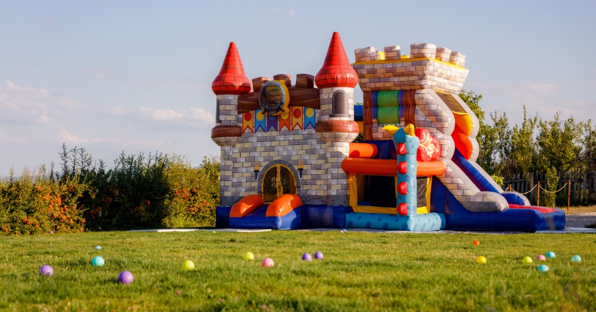 A tall bounce house shaped like a castle. The bounce house is surrounded by colorful balls outside during the daytime.